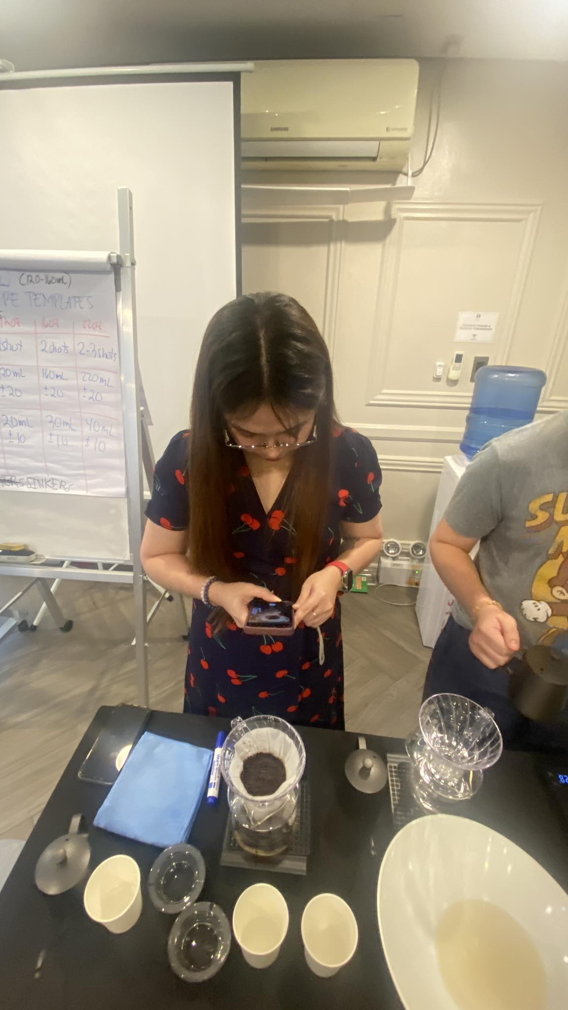 A participant brewing pourover beside the recipe board